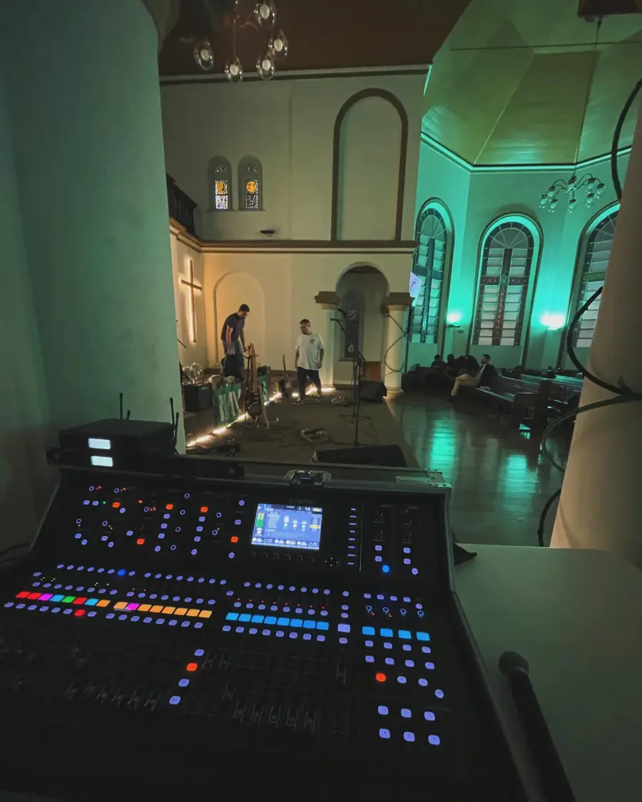 Mesa de som iluminada em igreja preparada para cerim&ocirc;nia de casamento com microfones e estrutura t&eacute;cnica montada