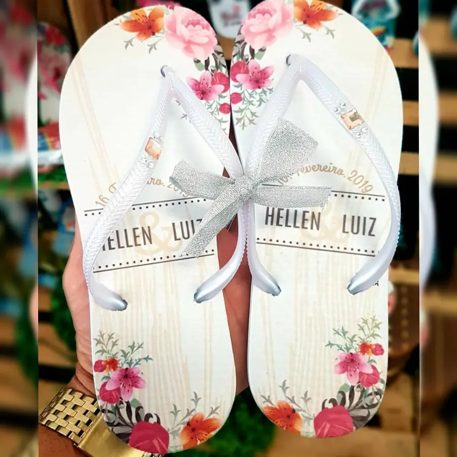 Chinelos personalizados brancos com flores coloridas, nomes Hellen e Luiz e laço prateado nas tiras.