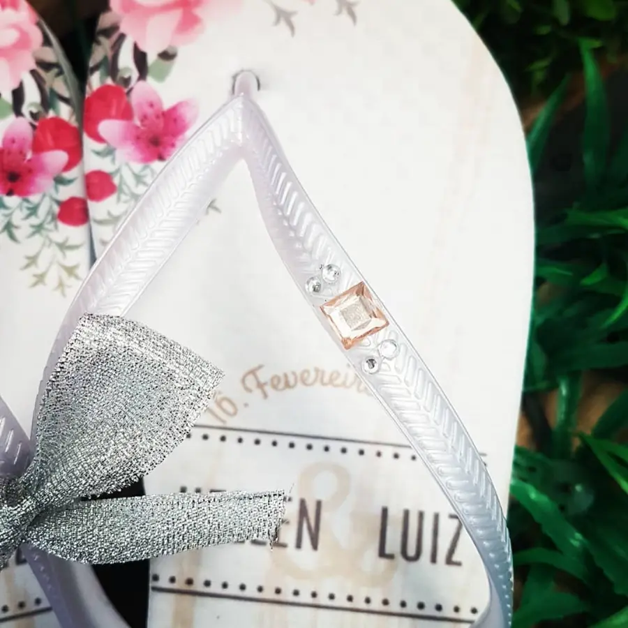 Detalhe de chinelo personalizado com tiras transparentes decoradas com laço prateado e pedrarias.