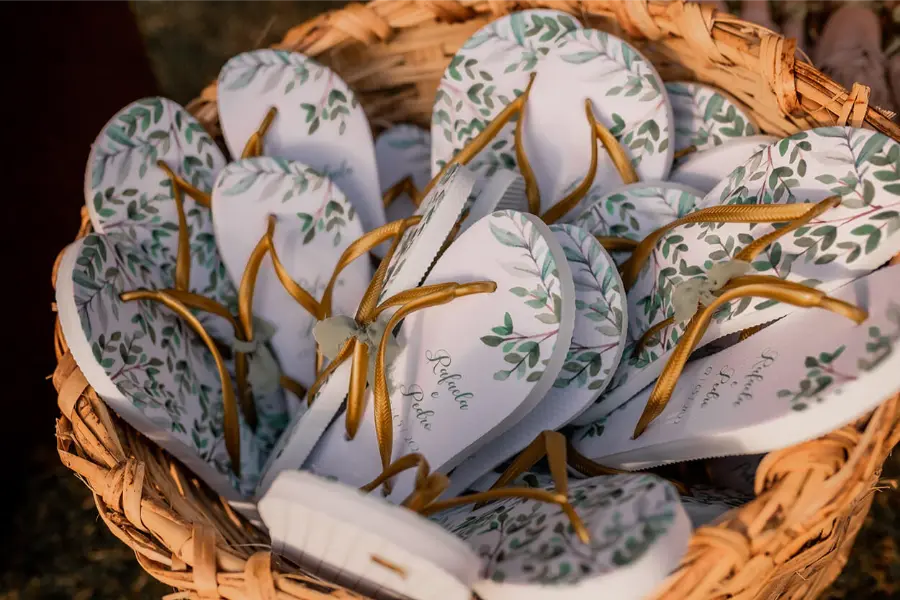 Cesta com chinelos personalizados de casamento estampados com folhagens verdes e tiras douradas.