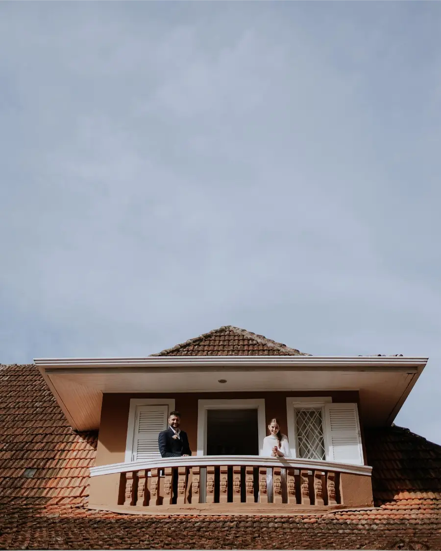 Casal de noivos posando na sacada de uma casa de telhado cerâmico,
