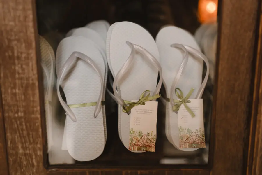 Chinelos personalizados brancos com tiras finas e tags decorativas, embalados para lembrancinha de casamento.