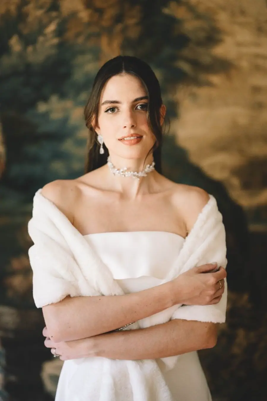 Noiva com cabelo preso e mechas soltas, usando vestido branco sem alças, choker de pérolas e estola de pele sintética branca.