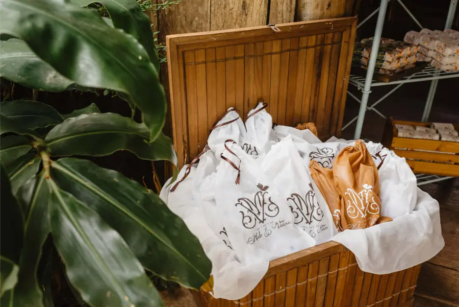 Chinelos personalizados de casamento embalados em sacos de tecido com monograma dos noivos dentro de baú de madeira.