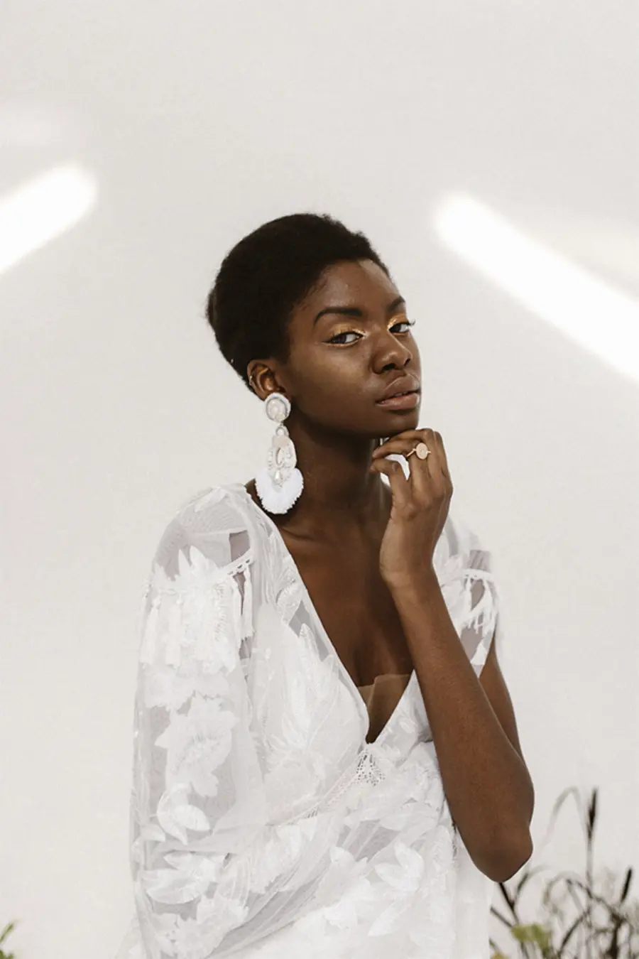 Noiva negra com cabelo curto natural, vestindo vestido branco com detalhes florais e brincos grandes brancos em formato de flor.