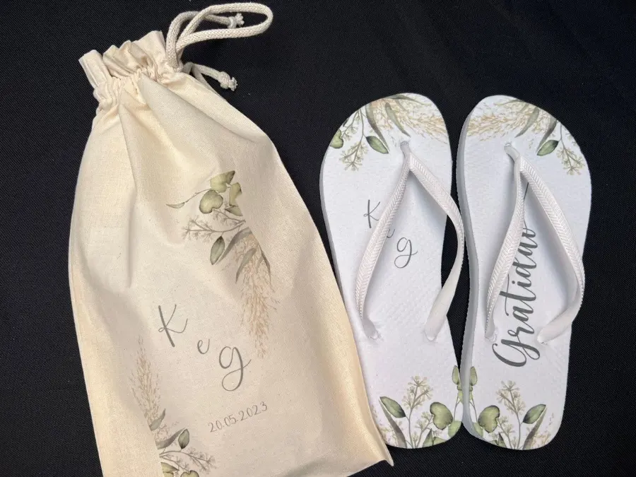 Chinelo personalizado branco com estampa botânica, embalado em saquinho de tecido com iniciais e data do casamento.