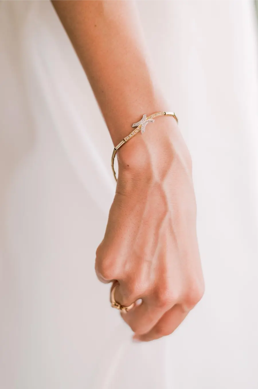Close da mão de noiva usando pulseira dourada fina com detalhe em forma de estrela cravejada de pedras e anel dourado.