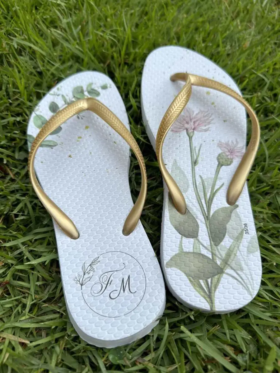 Chinelo personalizado branco com tiras douradas e estampa botânica delicada, iniciais J e M.