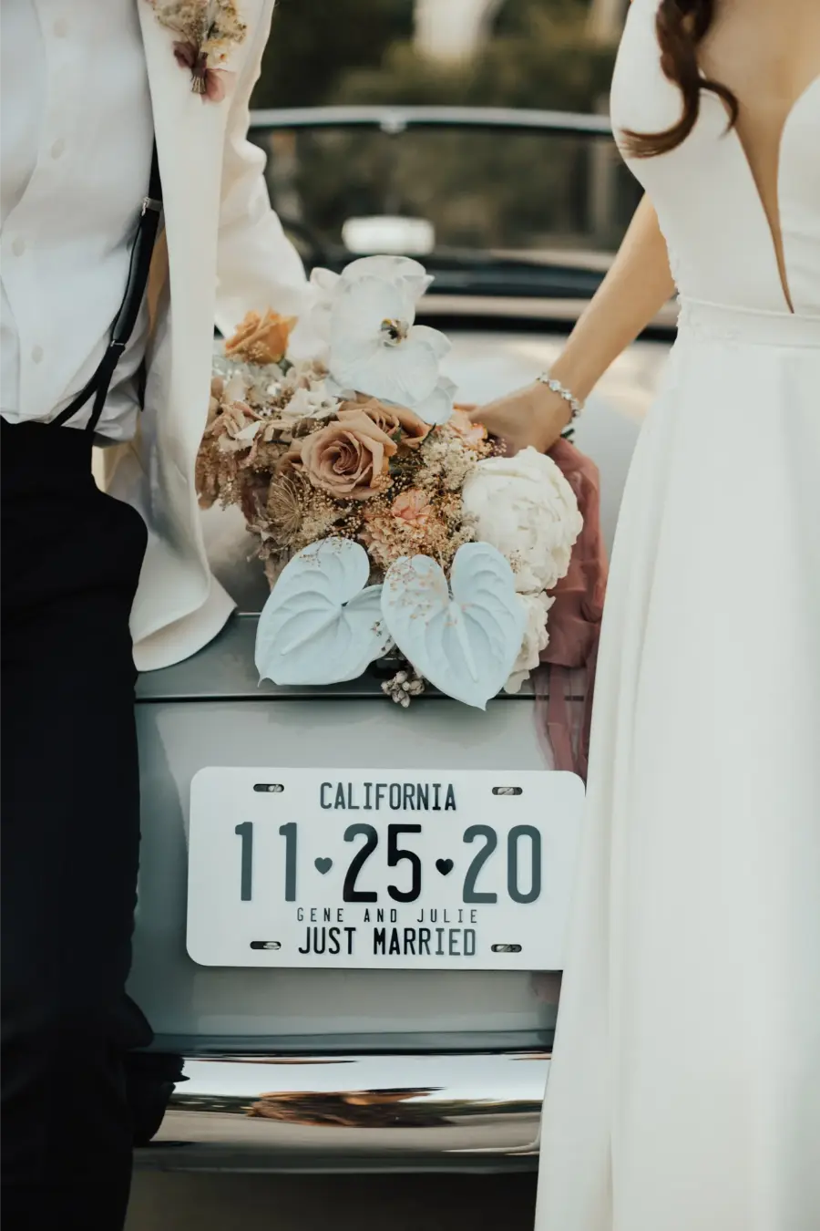 Detalhe de placa “Just Married” com buquê de flores apoiado na traseira de carro clássico prateado.