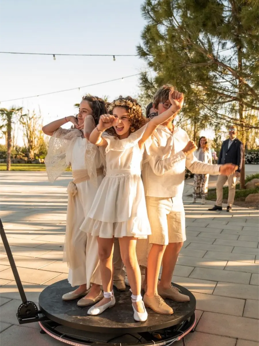 Crianças vestidas de forma elegante se divertindo em uma plataforma 360 ao ar livre durante evento de casamento.