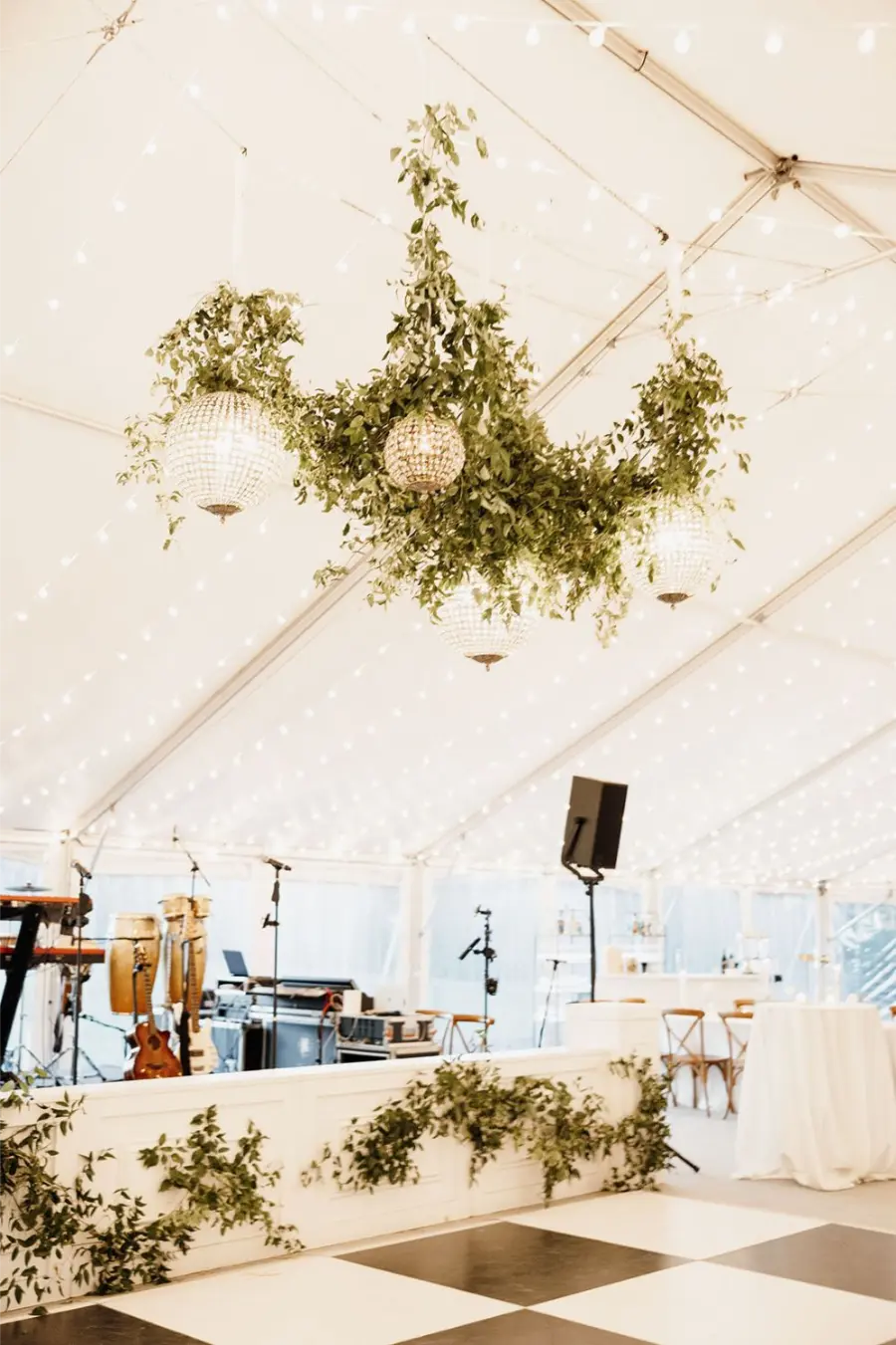 Palco decorado para festa de casamento com instrumentos, caixas de som e ilumina&ccedil;&atilde;o cenogr&aacute;fica sob teto de luzes.