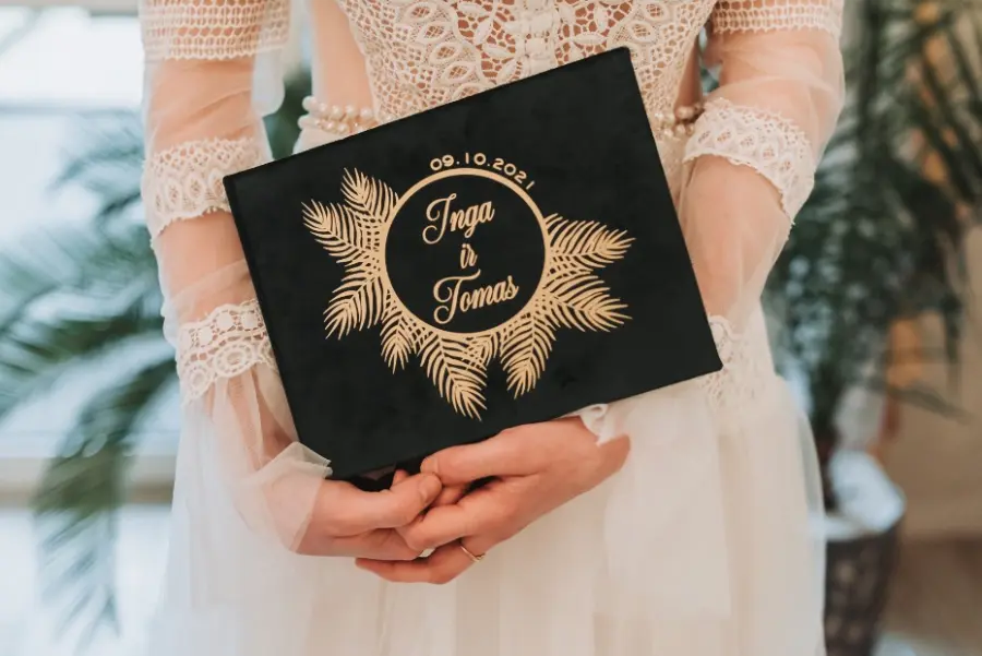 Noiva segurando livro de assinatura preto e dourado personalizado com nomes dos noivos e data do casamento.