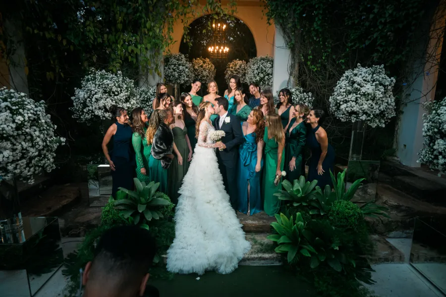 Noivos se beijando ao lado de madrinahs de verde petroleo