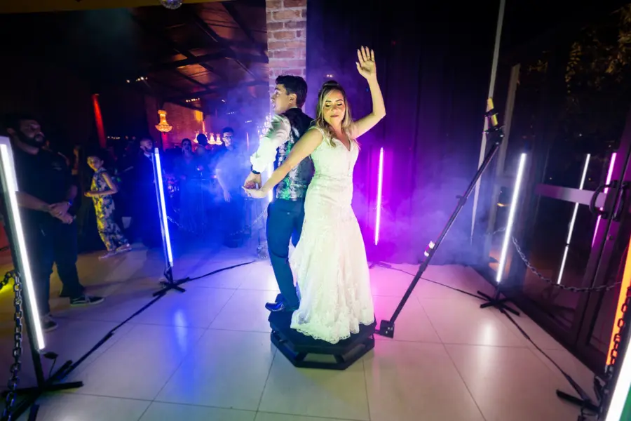 Casal de noivos dançando e posando em plataforma 360 com iluminação colorida e efeitos de fumaça, registrando momento especial do casamento.
