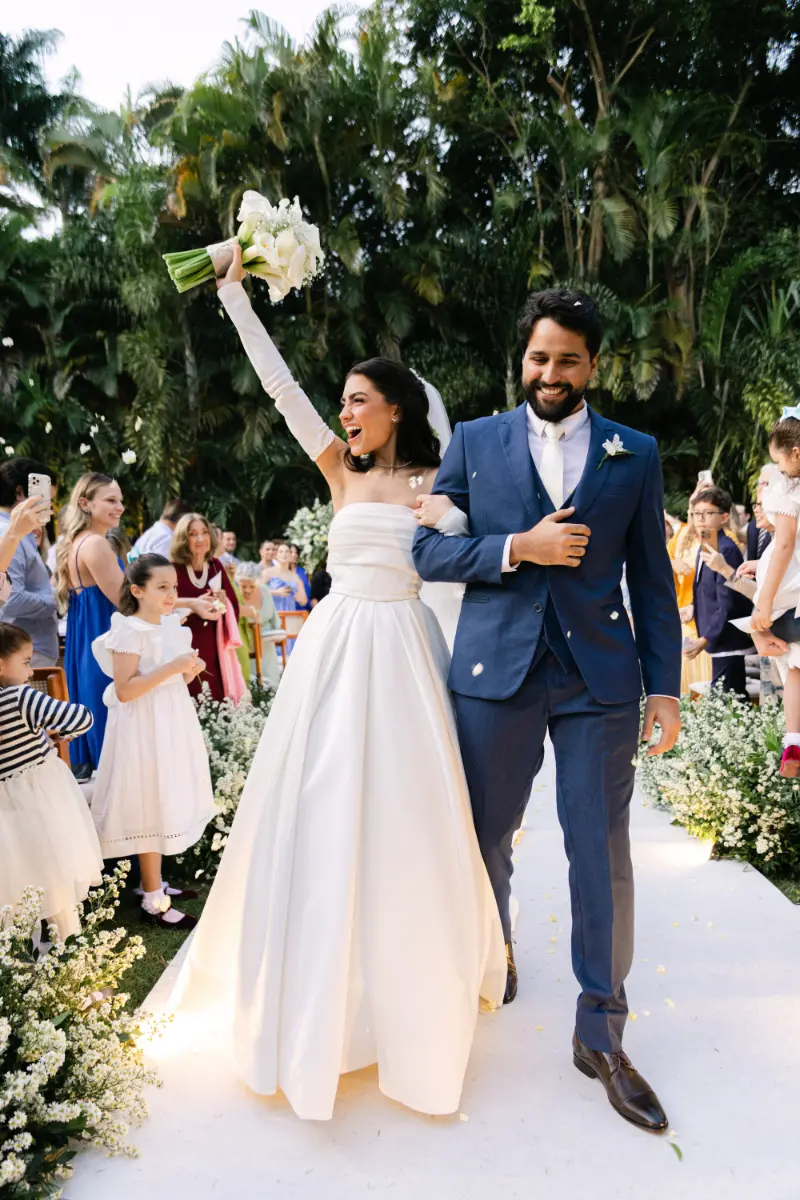 saída dos noivos com noiva levantando as mãos com o buquê enquanto caminha