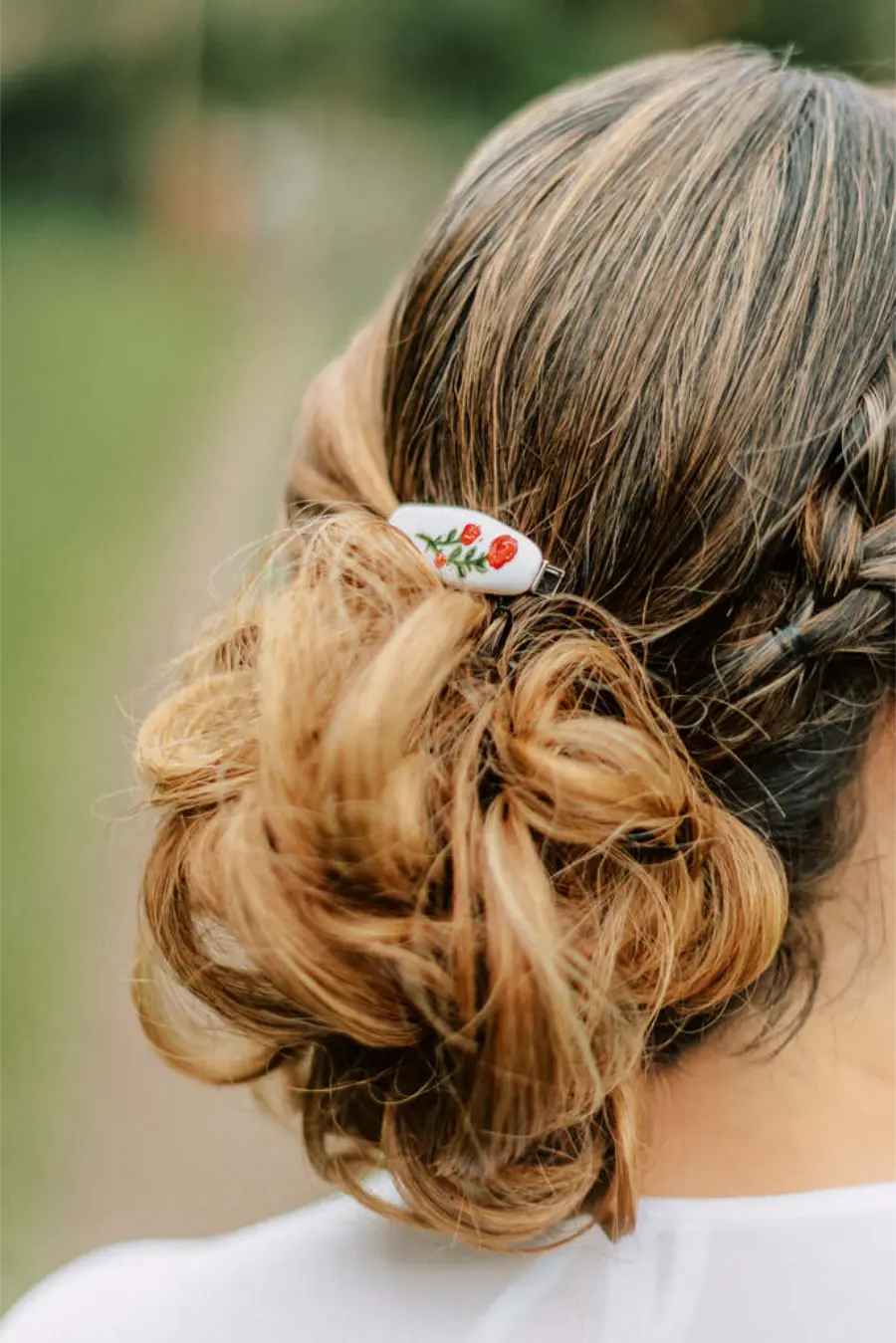 Coque baixo despojado com trança lateral e presilha floral em cabelo loiro.