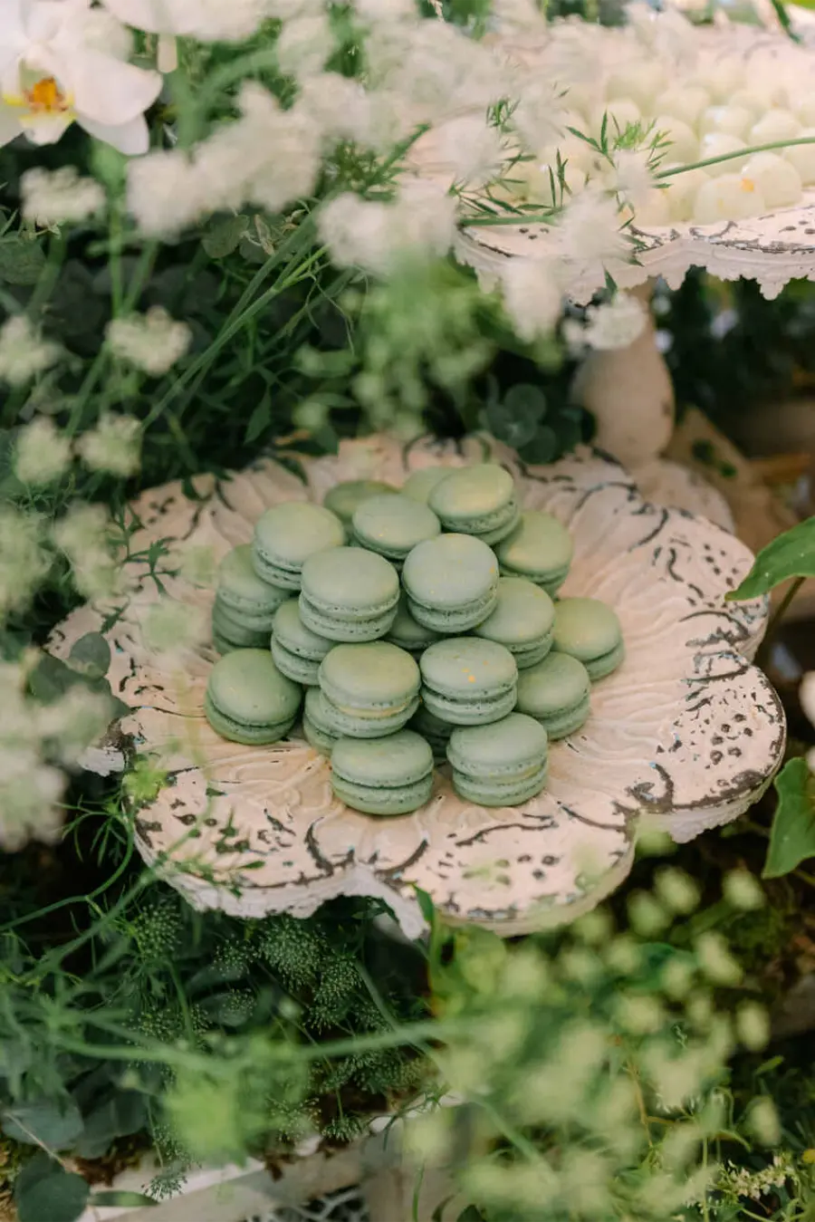 Prato rústico decorado com flores e folhas exibindo torre de macarons verdes em mesa de casamento ao ar livre.