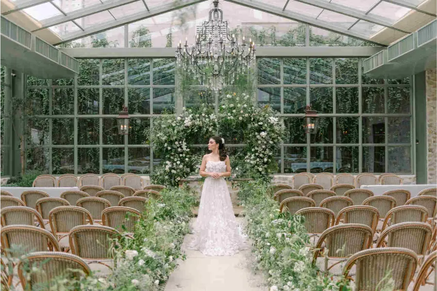 Espa&ccedil;o para casamento coberto com estrutura de vidro, lustre de cristal e decora&ccedil;&atilde;o floral branca. Noiva ao centro