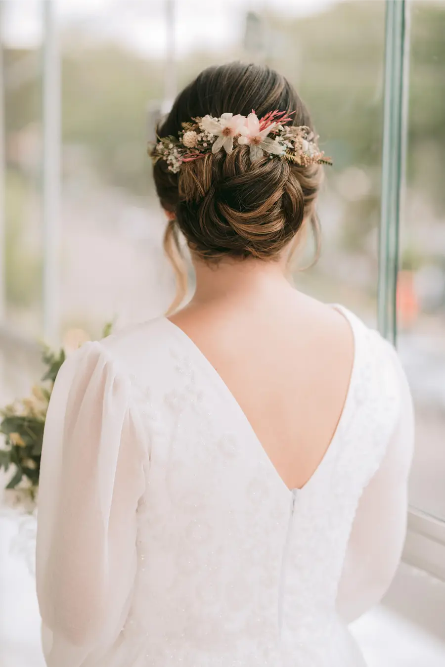 Noiva com coque baixo elegante adornado por coroa de flores secas.
