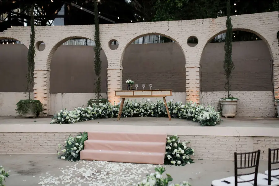 Altar de casamento em espa&ccedil;o com arquitetura de tijolos aparentes, arcos decorativos e arranjos florais brancos