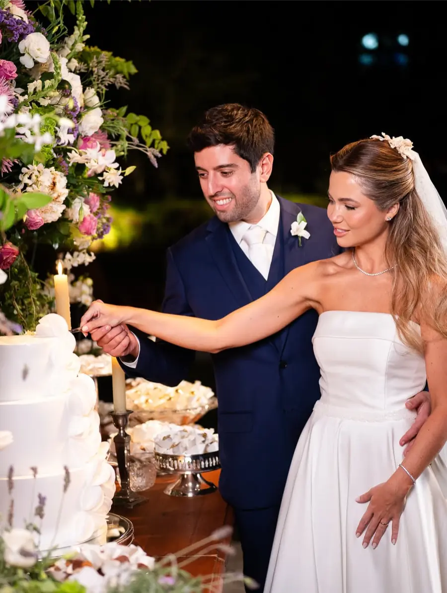 Noivos cortando bolo fake branco de três andares decorado com flores grandes em recepção elegante