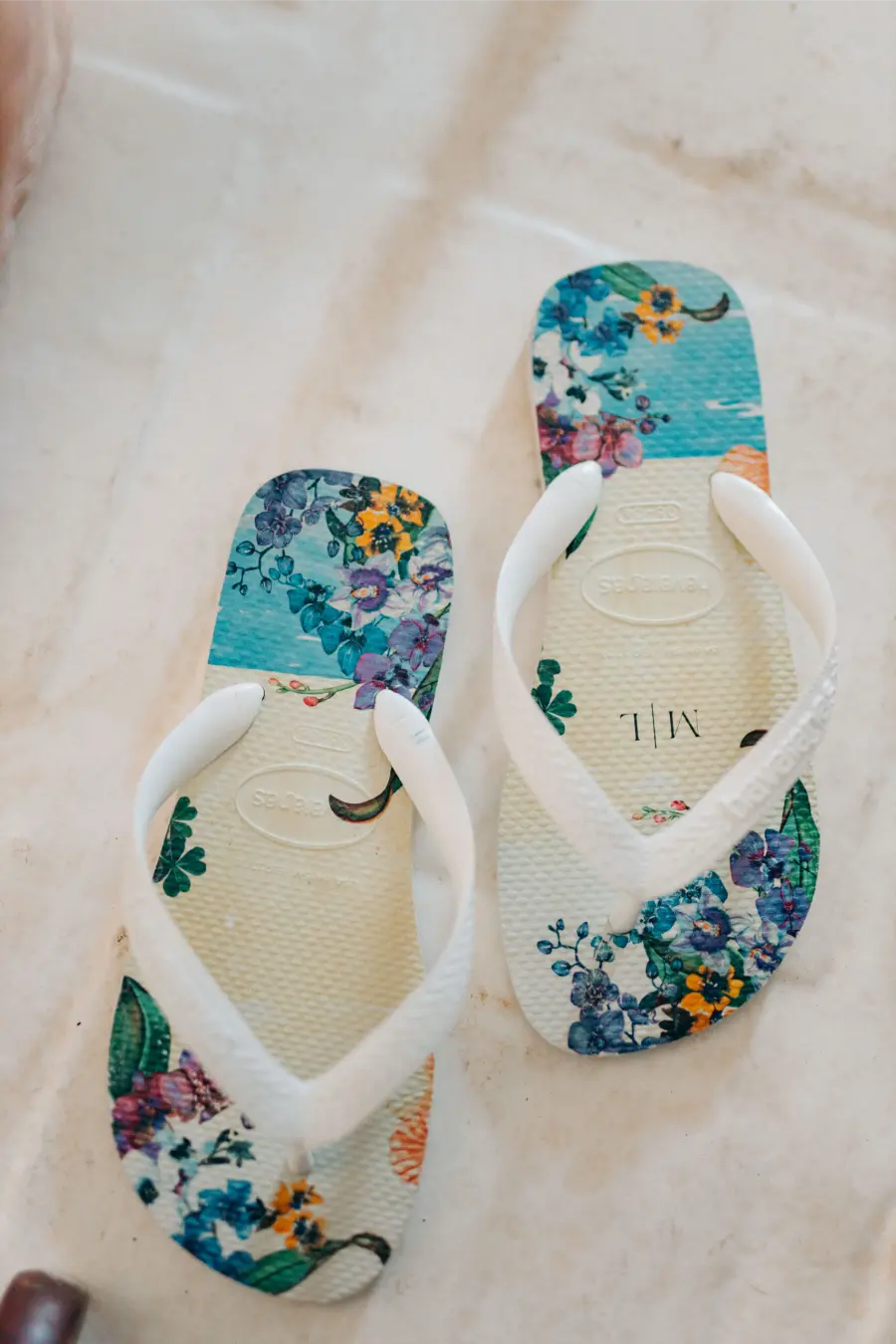 Chinelo branco personalizado com estampa floral em tons de azul, roxo e amarelo, lembrança delicada para casamento.