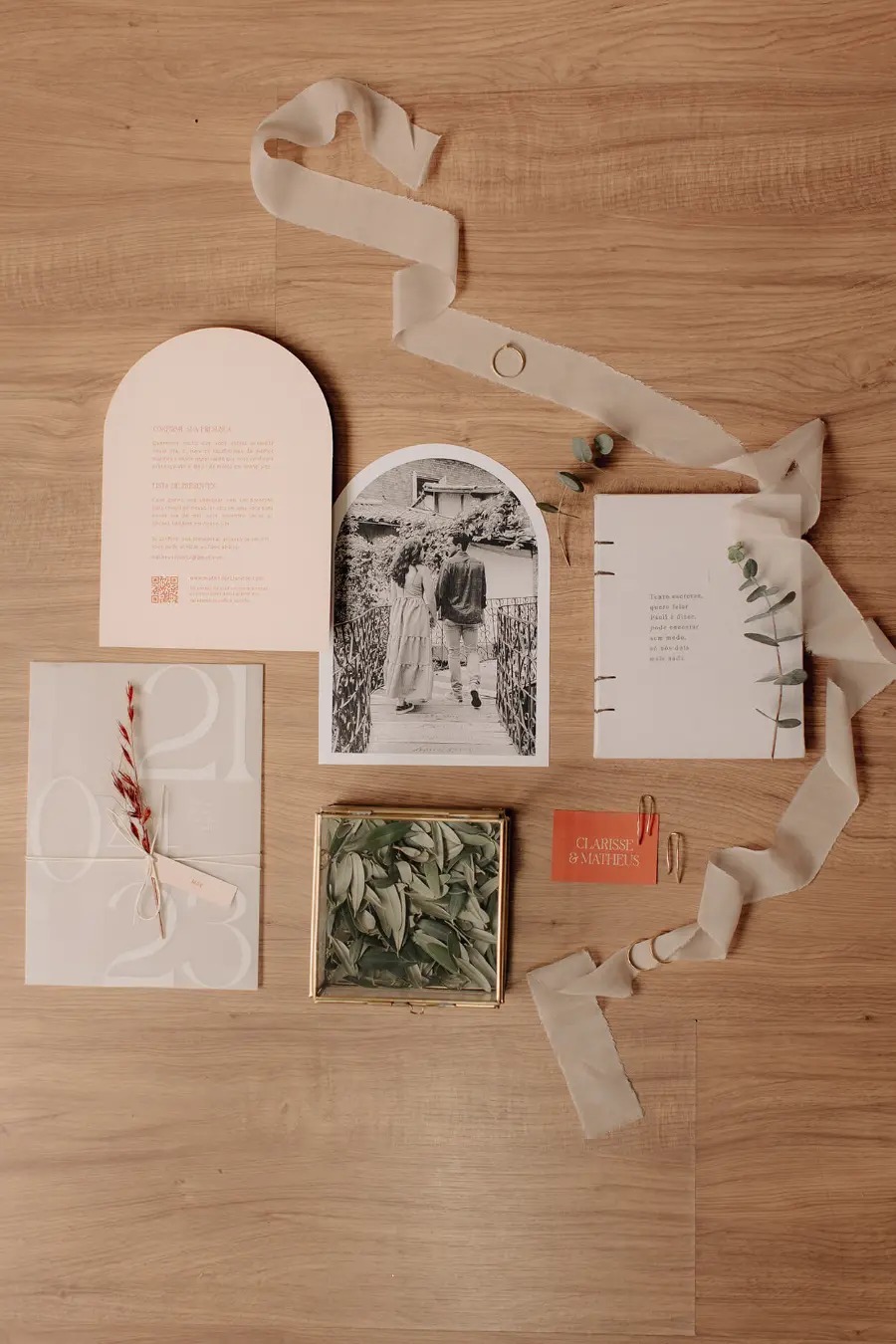 Convite de casamento moderno em tons claros com foto em preto e branco do casal e detalhes minimalistas, acompanhado de fita e folhagens secas.