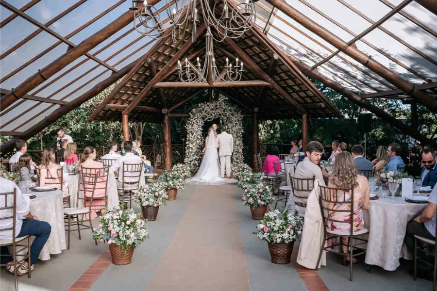 Cerim&ocirc;nia de casamento em capela coberta com estrutura de madeira, lustre de cristal e decora&ccedil;&atilde;o floral