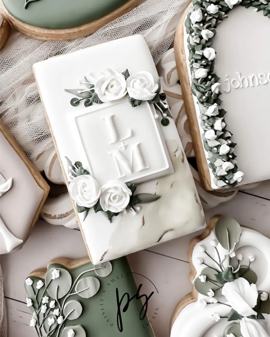 Biscoito decorado com glacê branco e flores artesanais, com iniciais dos noivos em relevo