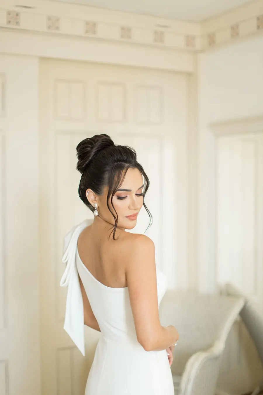 Noiva de vestido branco com coque alto sofisticado e mechas soltas na frente.