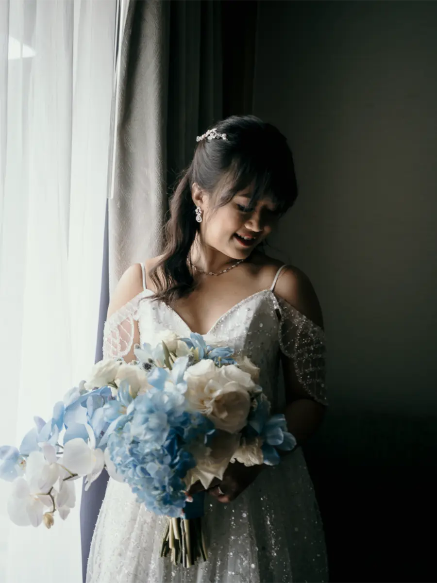 Noiva sorridente junto &agrave; janela segurando buqu&ecirc; em azul serenity e branco com orqu&iacute;deas