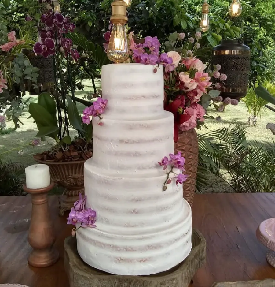 Bolo de casamento de quatro andares branco estilo semi-naked decorado com orquídeas roxas, em ambiente garden party com vegetação ao fundo