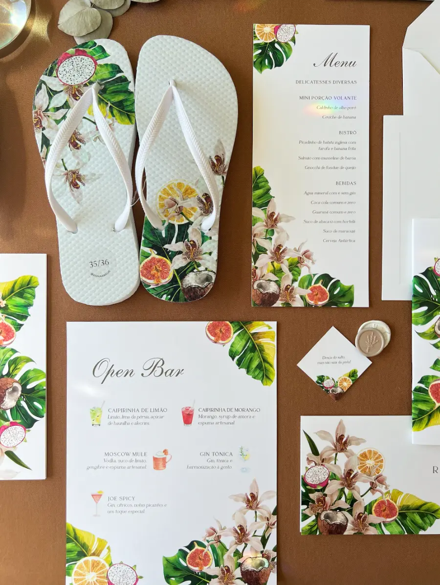 Kit de papelaria de casamento tropical acompanhado de chinelos personalizados brancos com estampa floral e frutal combinando.