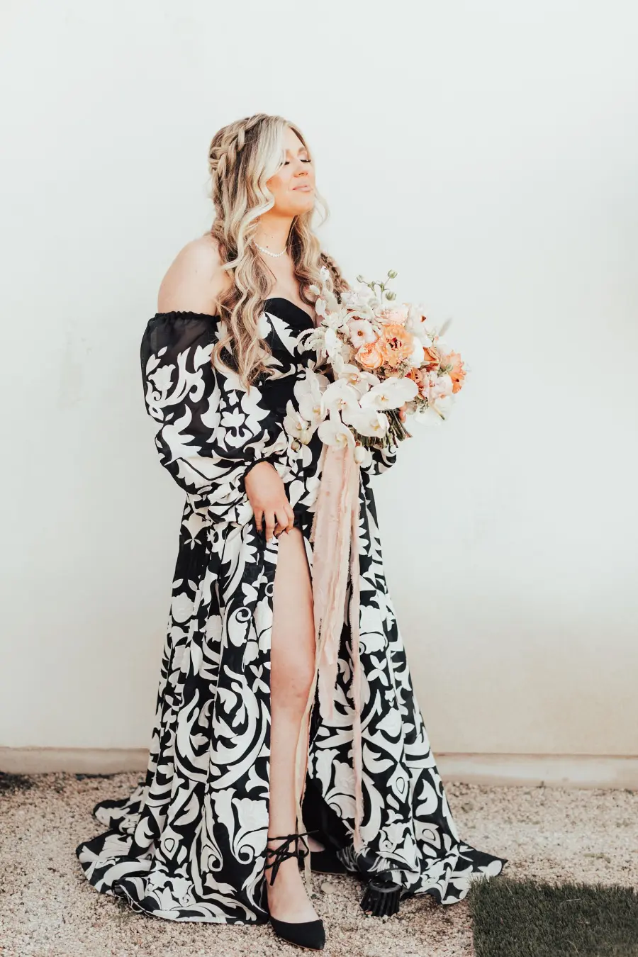 Noiva com vestido preto e branco estampado segurando buqu&ecirc; de flores claras.