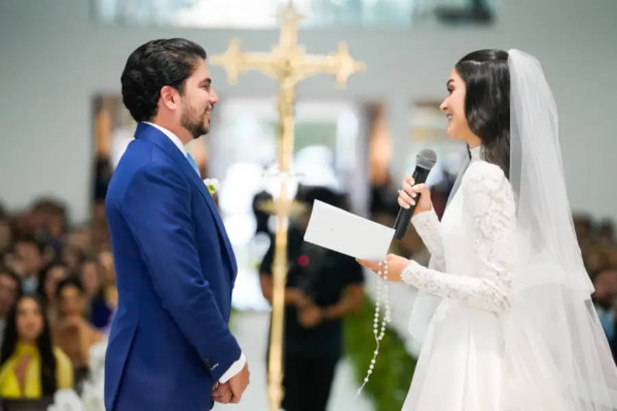 Noiva lendo votos no altar segurando terço nas mãos.