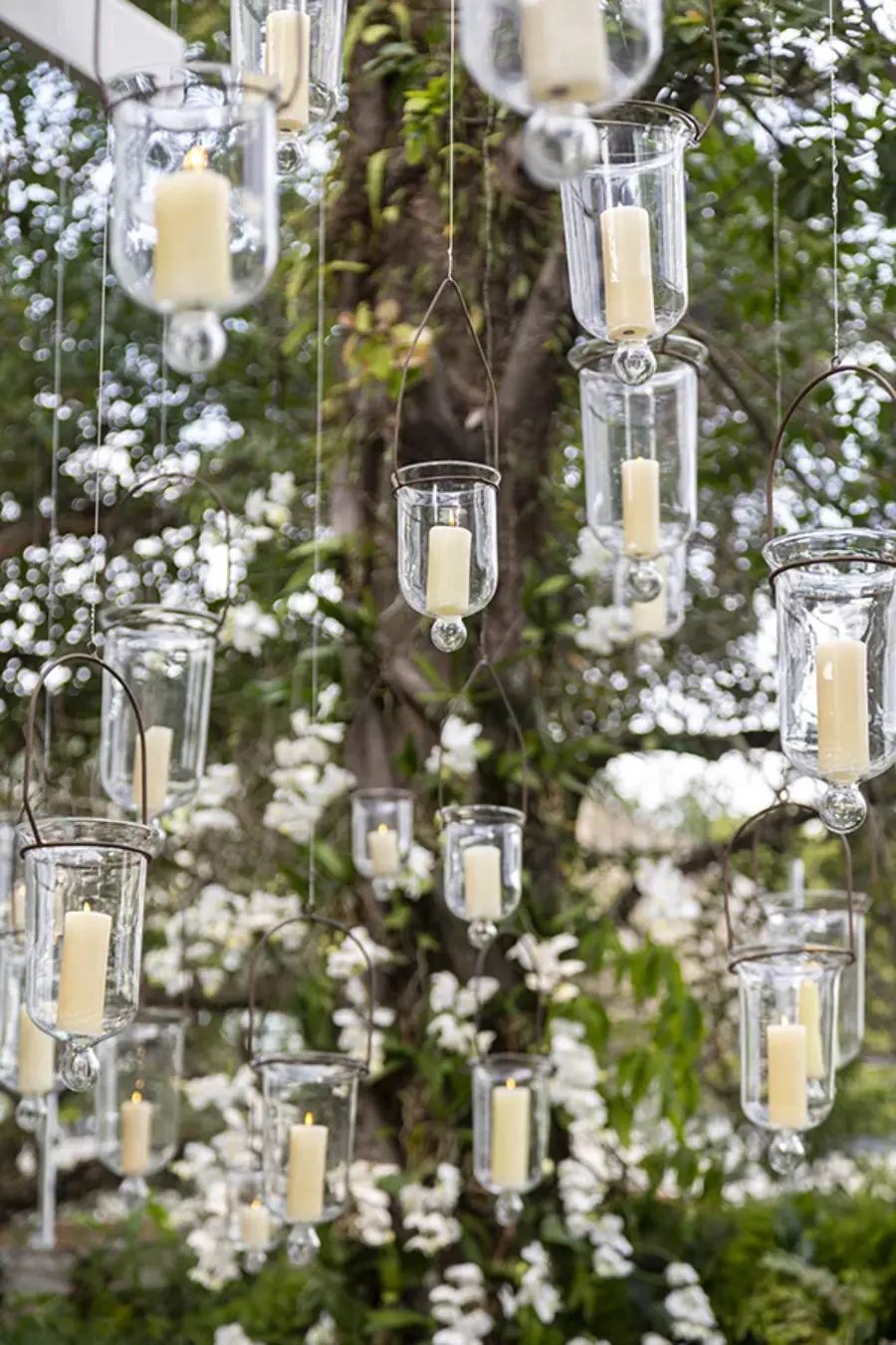 Velas suspensas em suportes de vidro pendurados em fios, decorando um espaço ao ar livre 