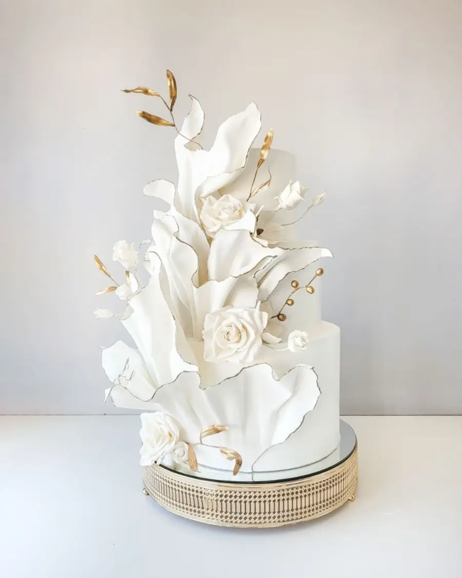 Bolo fake branco de dois andares decorado com flores e folhas brancas em arranjo artístico vertical