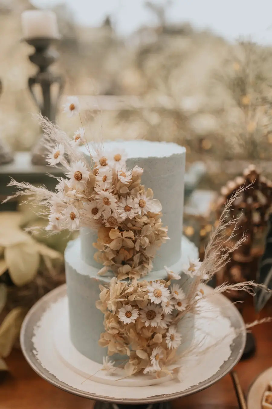 Bolo em tom azul claro decorado com flores secas e margaridas.