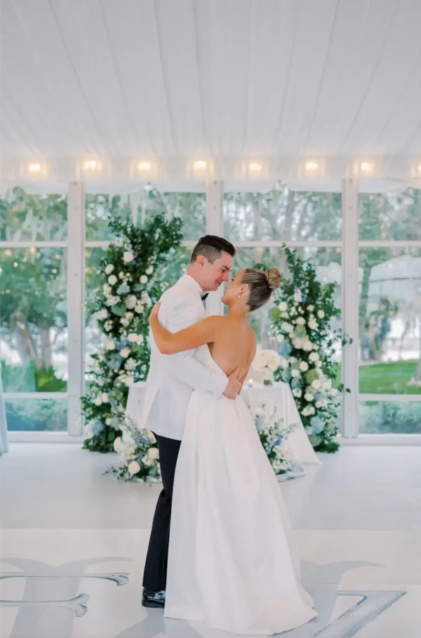 capa post: Casal de noivos dançando em salão decorado com flores brancas, noiva de coque alto.