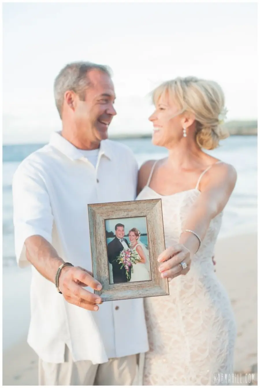 Casal sorridente mostrando foto do casamento antigo em porta-retrato durante ensaio na praia