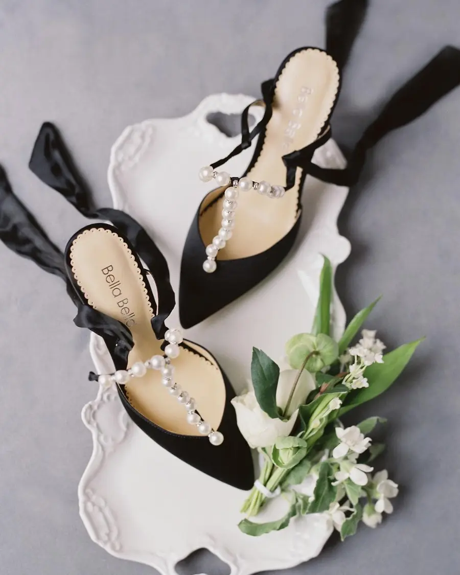 Sapatos pretos de noiva com detalhes em p&eacute;rolas sobre bandeja branca decorativa.