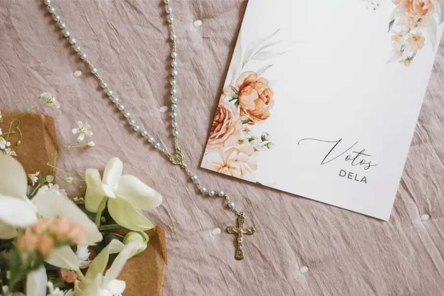 Terço prateado ao lado de caderno de votos com capa floral.