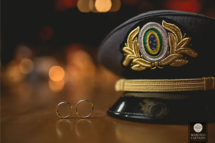 Alian&ccedil;as douradas posicionadas ao lado de quepe militar com bras&atilde;o do Brasil em detalhe cerimonial de casamento.