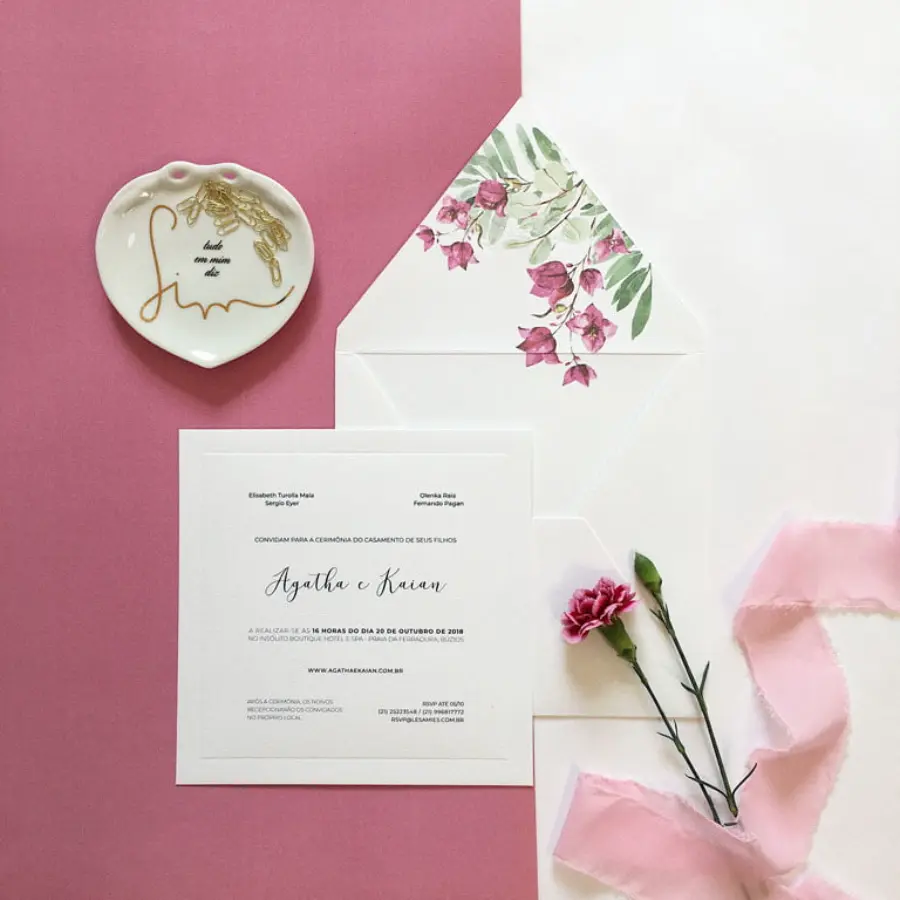Convite de casamento quadrado branco com envelope forrado de flores cor-de-rosa, decorado com fita de tecido e flor natural.