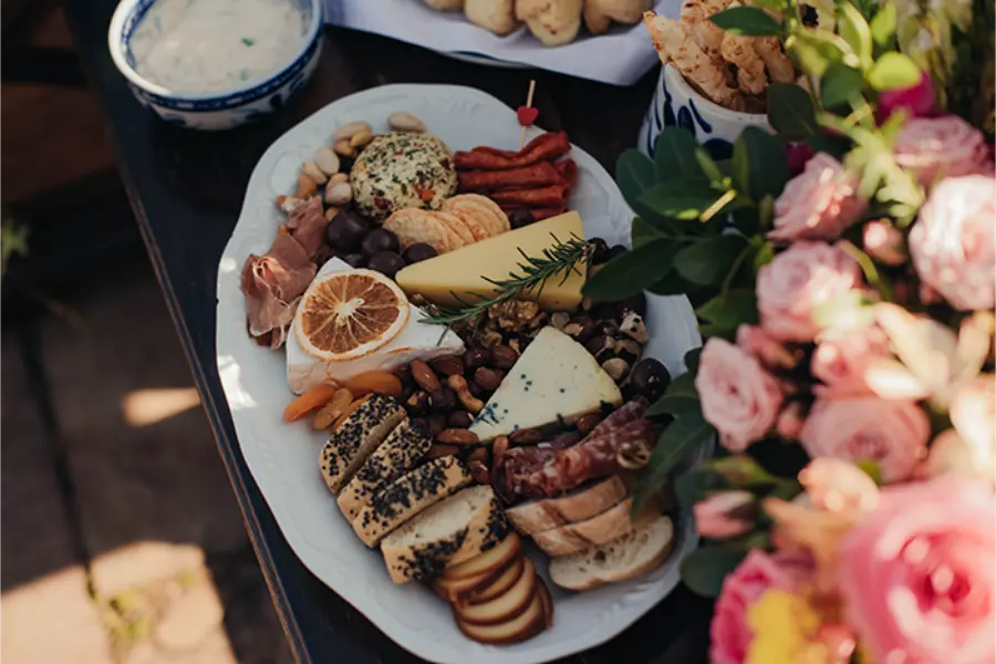 Mesa de casamento simples ao ar livre com tábua de frios, queijos, pães e frutas secas decorada com flores.