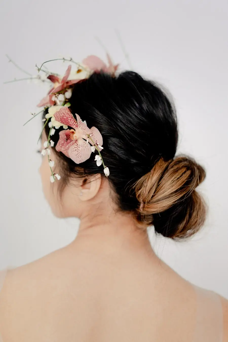 Coque baixo descontraído com flores cor-de-rosa e brancas como acessório de cabelo de noiva.