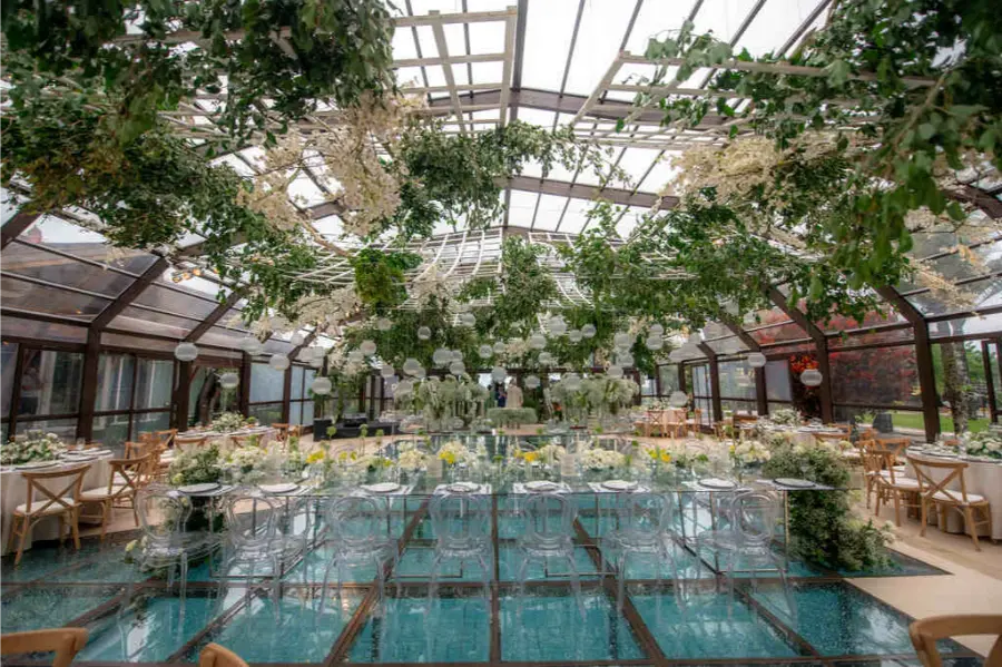 Sal&atilde;o de festa para casamento em estufa de vidro com piscina central e decora&ccedil;&atilde;o suspensa de flores