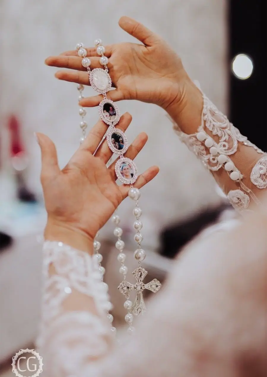 Noiva segurando terço de pérolas com relicários contendo fotos de familiares.