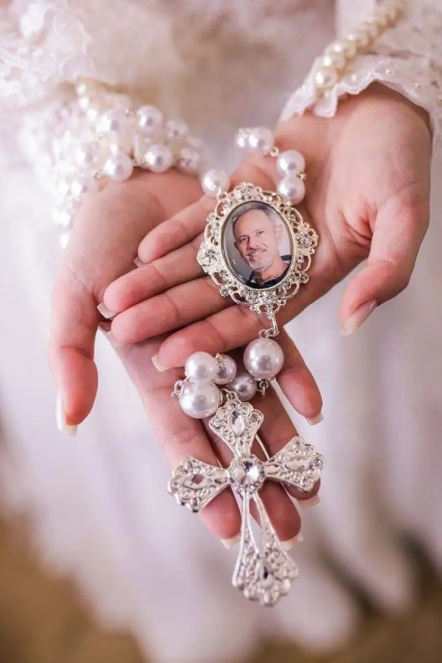 Noiva segurando terço de pérolas com relicário contendo foto masculina.