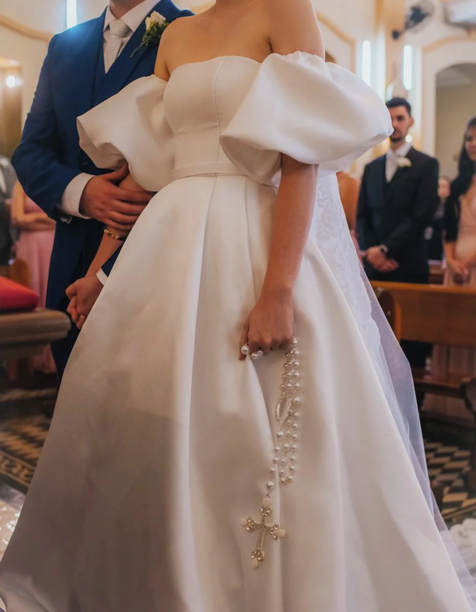 Noiva em cerimônia segurando um terço de contas médias brancas com crucifixo prateado.